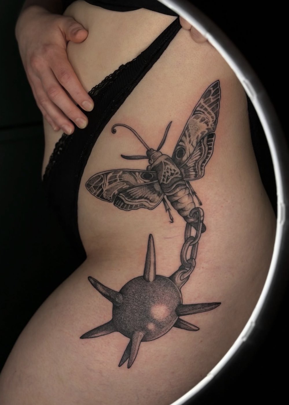 Surreales Tattoo an der Hüfte: Nachtfalter mit Morgenstern an der Kette – gestochen von Florian Rudolph in Berlin