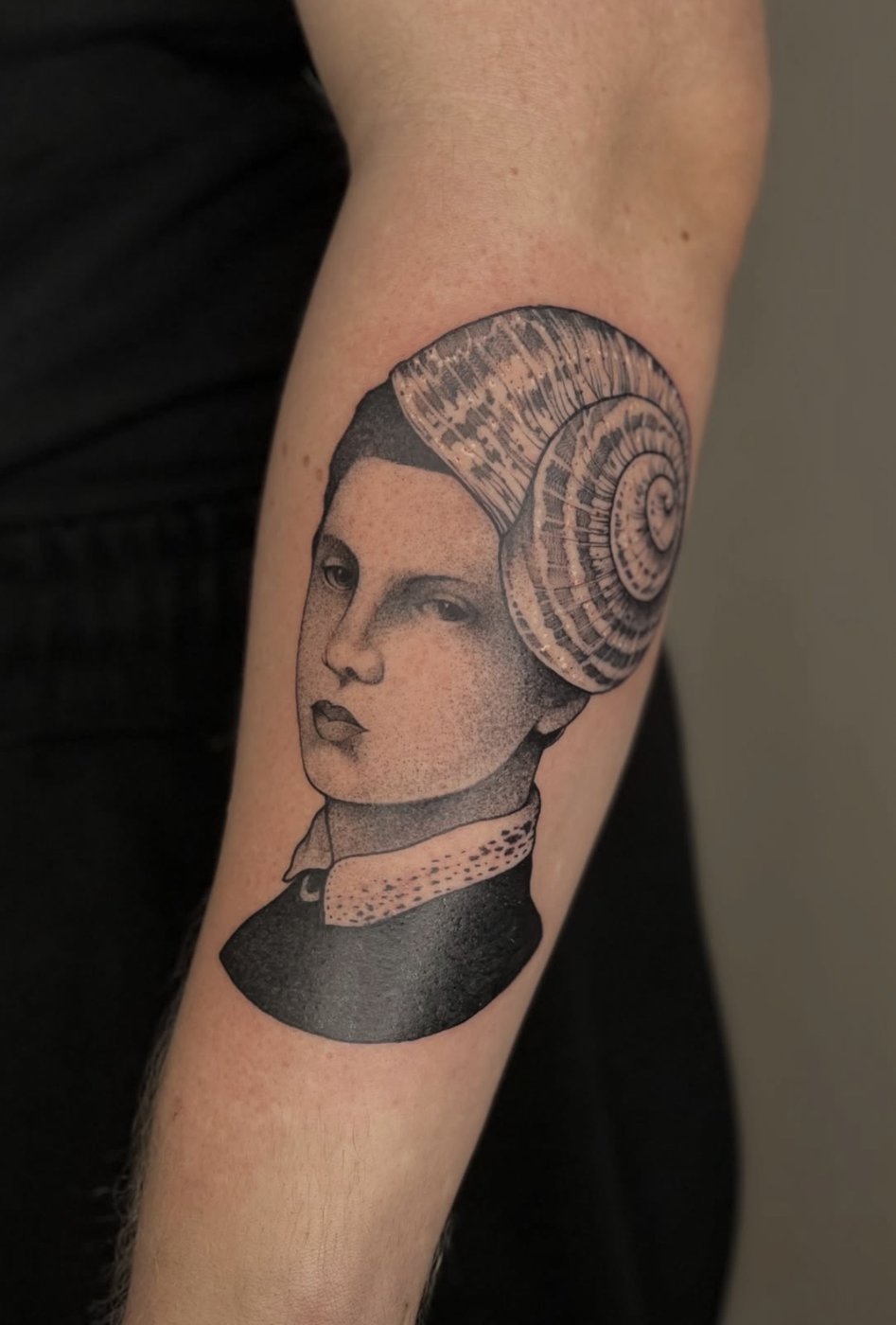 Surreales Tattoo am Unterarm: Frauenporträt mit Schneckenhaus als Frisur – gestochen von Florian Rudolph in Berlin