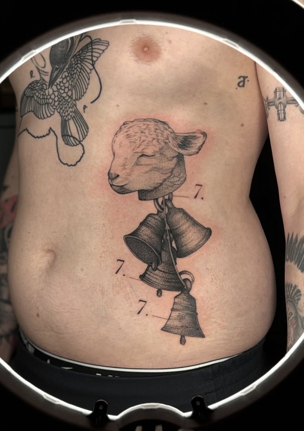 Surreales Tattoo am Bauch: Lammkopf, aus dem Glocken wachsen – gestochen von Florian Rudolph in Berlin